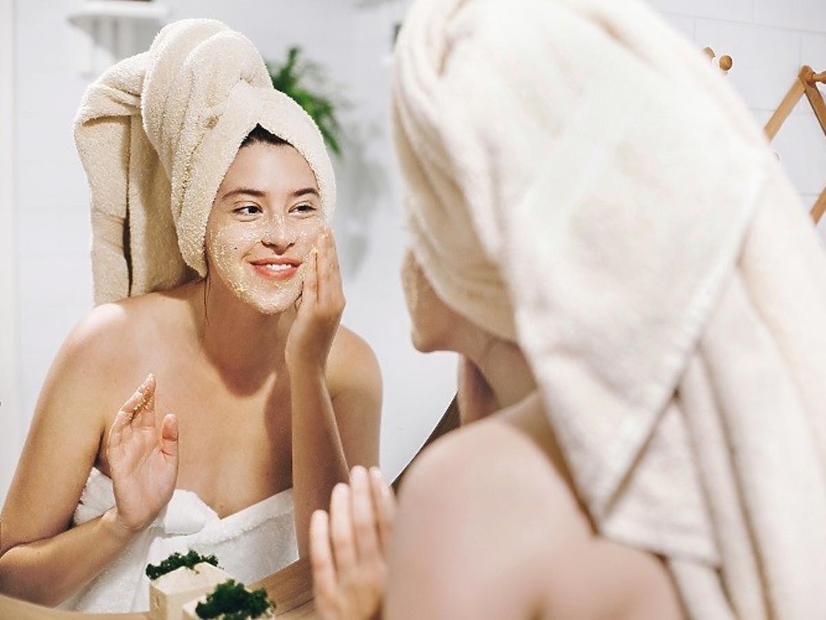 Kobieta w turbanie z ręcznika stoi przed lustrem 