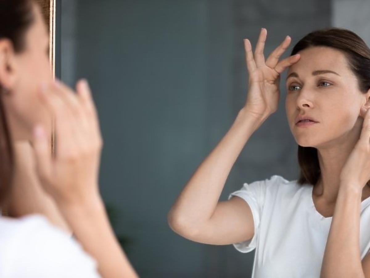 Niespokojna kobieta patrząca w lustro, dotykająca czoła, zd